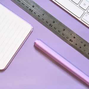 Flat lay of a pastel-colored workspace featuring a notebook, ruler, highlighter, and keyboard.