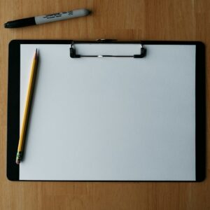 Clipboard, pencil, and pen on a wooden surface.